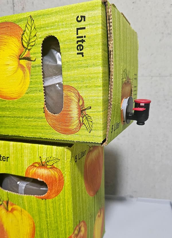Zwei gestapelte Bag-in-Box-Kartons mit Apfelmotiv, beschriftet mit „5 Liter“, am oberen der rote Zapfhahn.